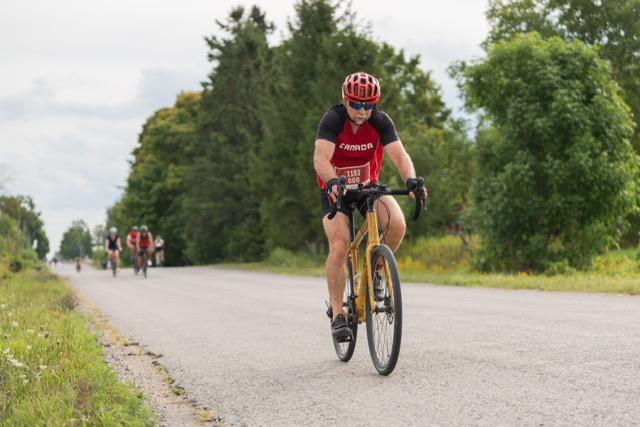 Bob Berezowski cycling on a country road in a Canada jersey during a duathlon, representing his enduring commitment to active living, strength and competition in his 60s