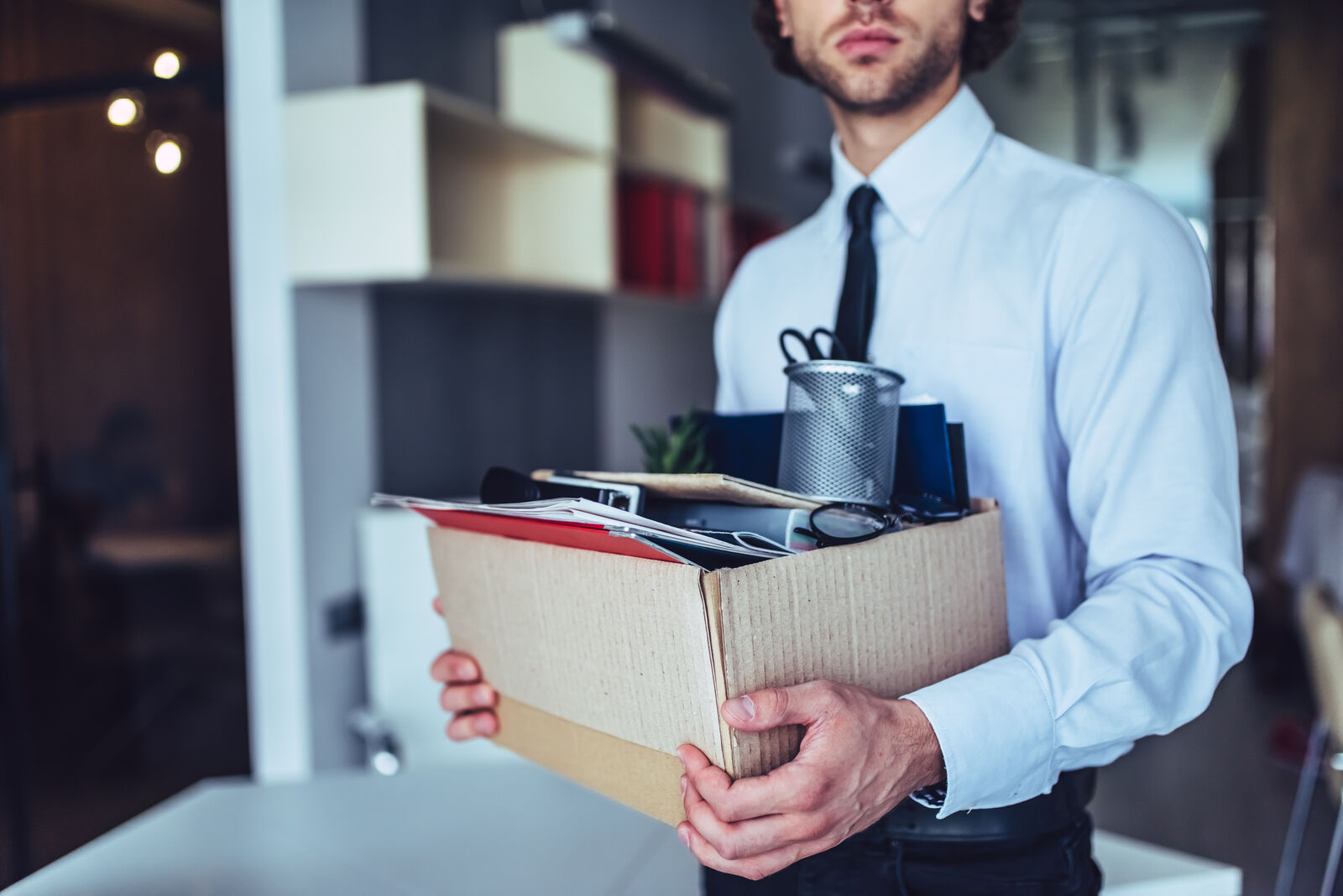 Man in a white shirt and tie carrying a cardboard box of personal belongings out of an office after losing his job. Man in a white shirt and tie carrying a cardboard box of personal belongings out of an office after losing his job.