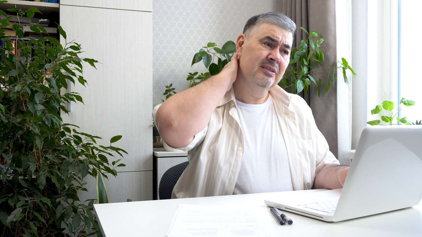 Man at a desk holding his neck in discomfort from long hours of office work. Man at a desk holding his neck in discomfort from long hours of office work.