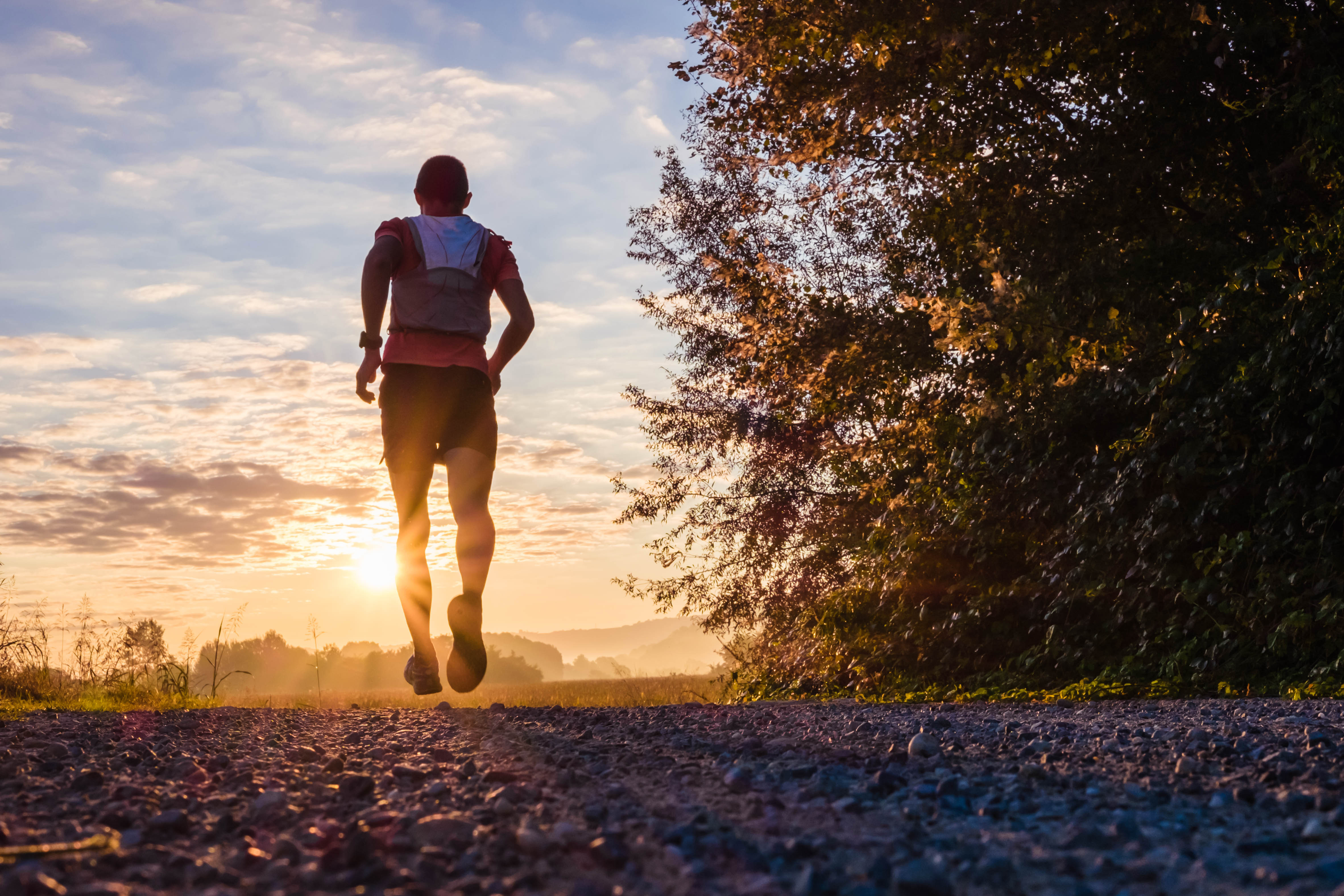 Man running on a dirt path in the evening, as the sun sets Man running on a dirt path in the evening, as the sun sets