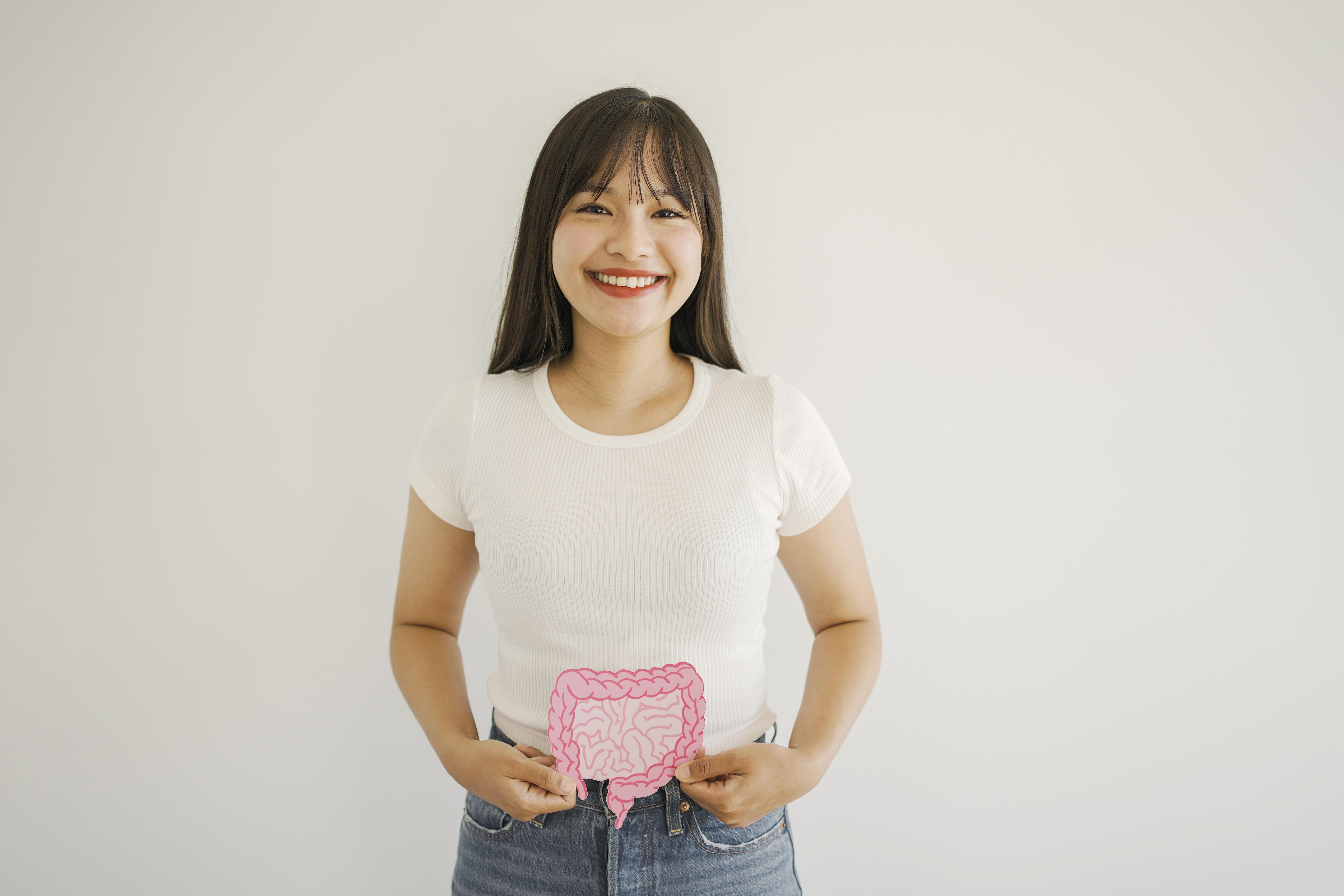 Young woman smiling at camera wearing white ribbed t-shirt with pink intestinal system graphic on abdomen and blue jeans.