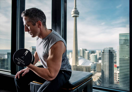 Man doing a bicep curl at the Toronto Athletic Club in front of the CN Tower