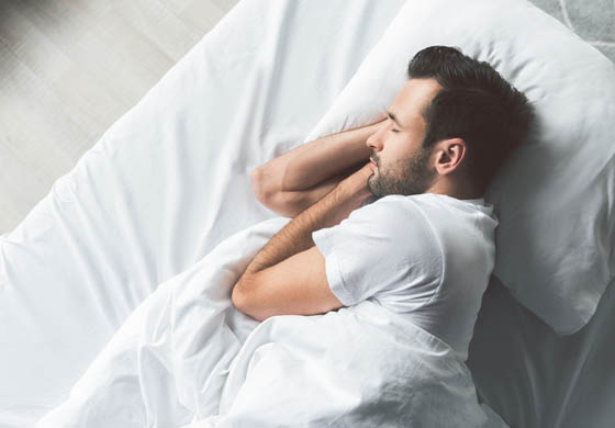 Young man sleeping on his side in a bed with white sheets