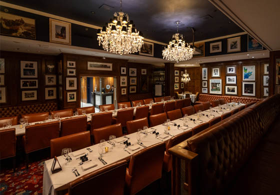 Oak Room at the Cambridge Club set-up for a large formal event - long tables set for the event, chandeliers on the ceiling, and artwork on the walls.