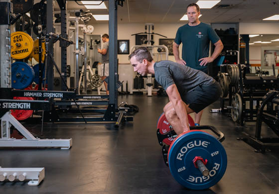 Fit man lifting weights on the gym floor at the Cambridge Club with a personal trainer