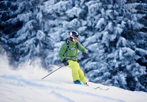 Young man in a green snowsuit, skiing down a snowy slope